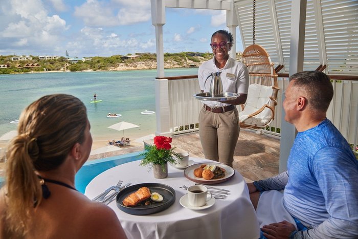 A couple walking the beach with drinks in hand at Hammock Cove Antigua