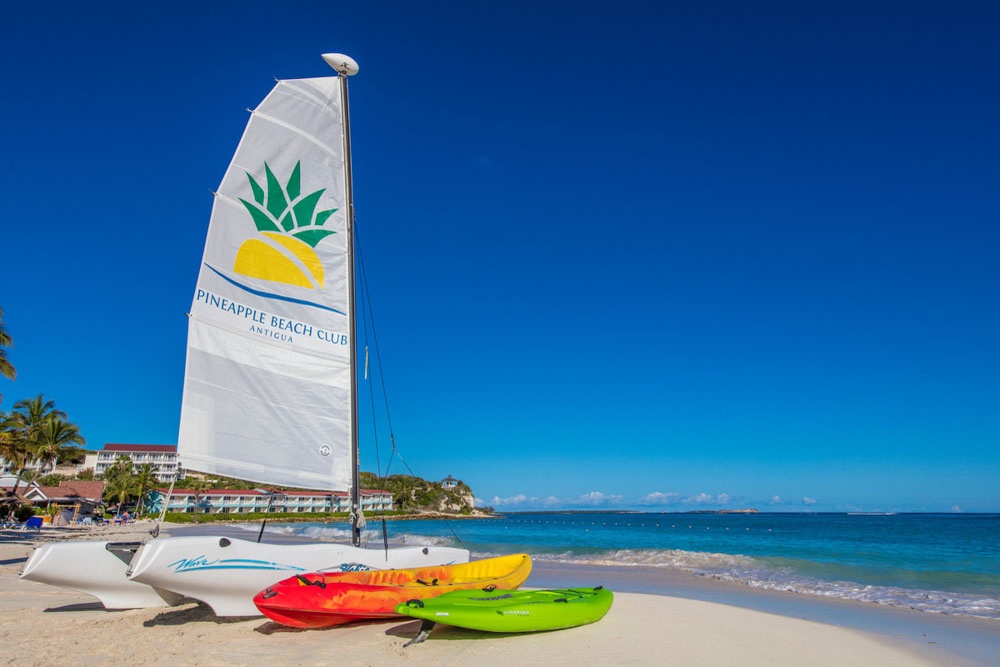 Hobie Cat sailboats and kayaks lined up on the white-sand beach at Pineapple Beach Club Antigua